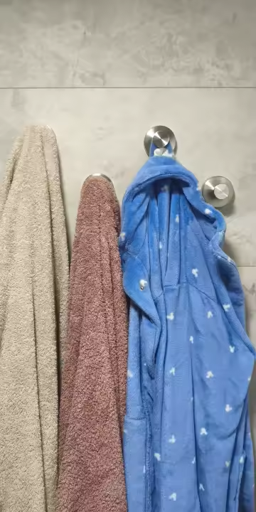 Silver suction hooks holding towels and a blue dressing gown